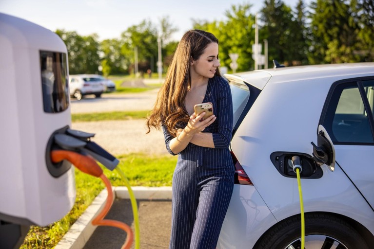 Young woman leans against her car that is currently charging