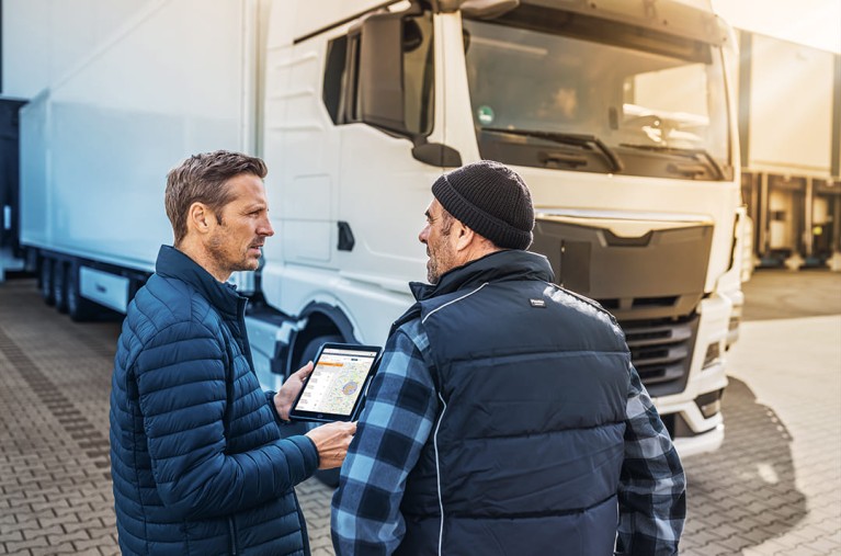 Two men in front of truck with Ipad and digital assistant