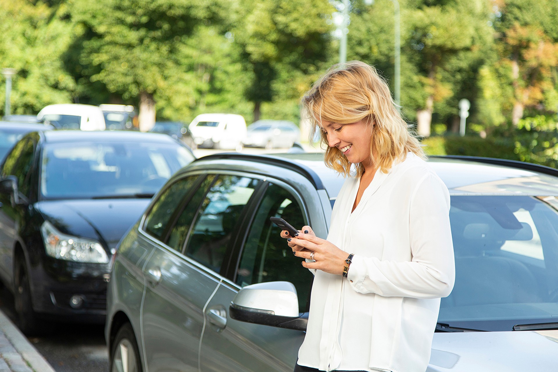 Frau lehnt an ihrem Auto und schaut auf Handy in ihrer Hand. Frau lehnt an ihrem Auto und schaut auf Handy in ihrer Hand.