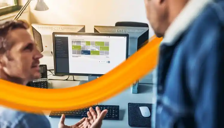 two persons speaking in front of a desktop showing the fleet management tool