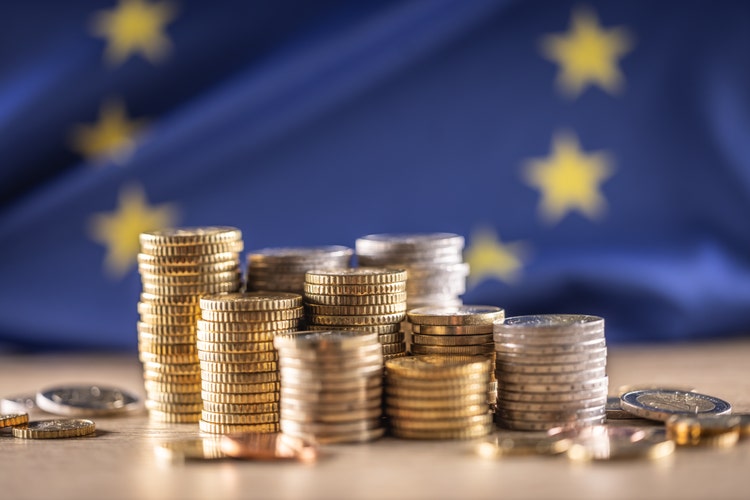 Euro coins stacked on top of each other in different positions in front of the flag of the European Union. Finance Business and Economy Concept.