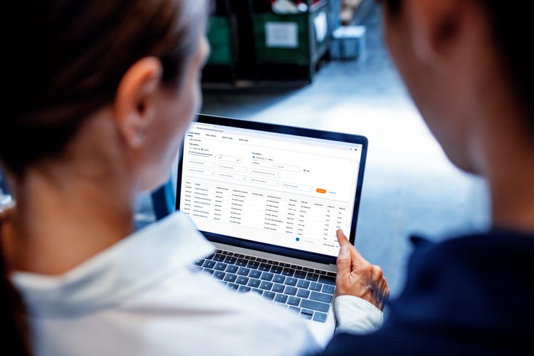 Young woman showing stock level to a worker in warehouse on a laptop computer. Warehouse manager with worker verifying stock level on system.