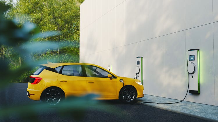 Electric car charging at a modern charging station beside a building surrounded by greenery.