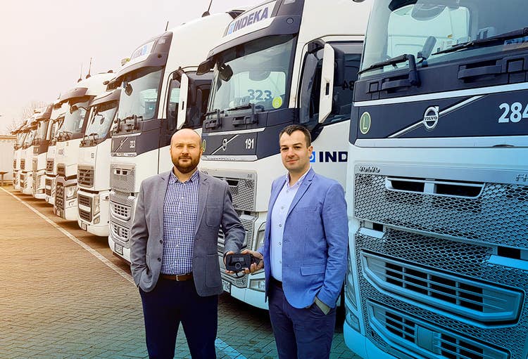 Two man in front of IDEKA trucks holding up an EETS box.